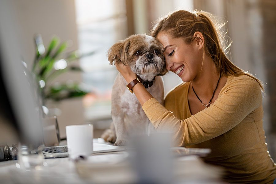 Refer a Pet Business - Closeup View of a Smiling Woman Sitting in Her Office Cuddling with Her Dog